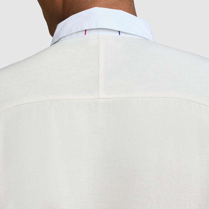 Close-up of the back of a person wearing a white Long Sleeve Rugby Shirt with Twill Collar from Champion, featuring a visible seam and subtle blue and red stitching near the collar, evoking classic rugby shirt details with an embroidered C logo.