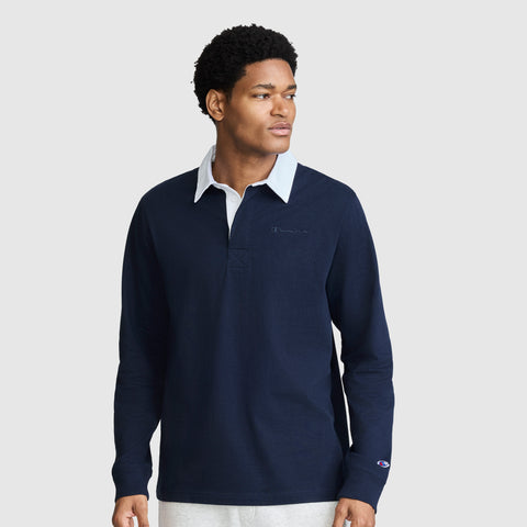 A man wearing the Champion Long Sleeve Rugby Shirt with Twill Collar and Embroidered C Logo in navy, featuring a white collar, stands against a plain light background, looking to his left with a neutral expression.