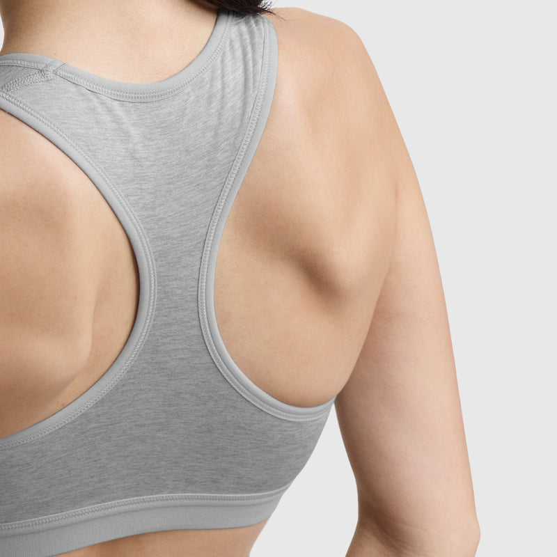 Close-up of a woman’s upper back and shoulder in the Champion Compression Sports Bra, C Logo, light gray. Moderate support and moisture-wicking fabric keep you comfortable during workouts against a plain background.