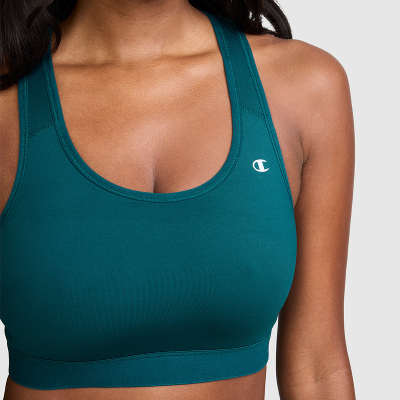 A woman wearing the Champion Compression Sports Bra, C Logo in teal, designed for moderate support with moisture-wicking fabric and the Champion logo on the left side, shown from shoulders to upper waist against a plain background.