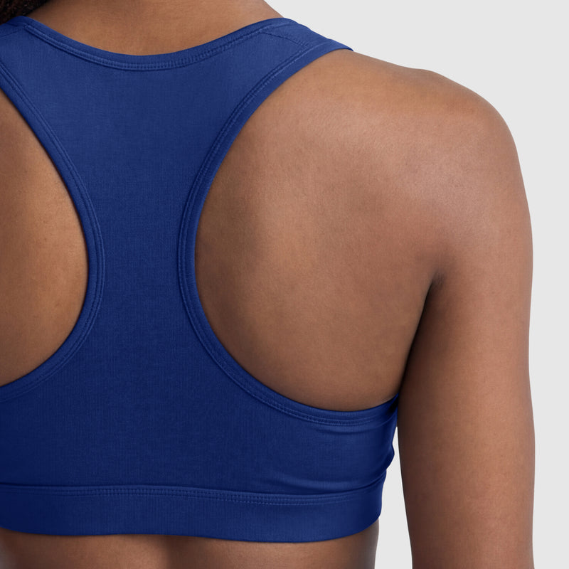 A close-up of a person’s upper back and shoulders wearing the Champion Compression Sports Bra with C Logo in blue, shown against a plain light background.