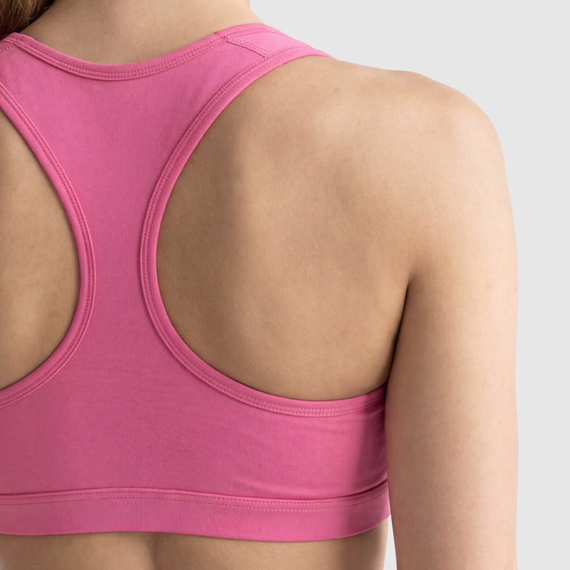 A close-up of a person’s upper back wearing the Champion Compression Sports Bra, C Logo, in pink with moderate support, shown against a plain light gray background.