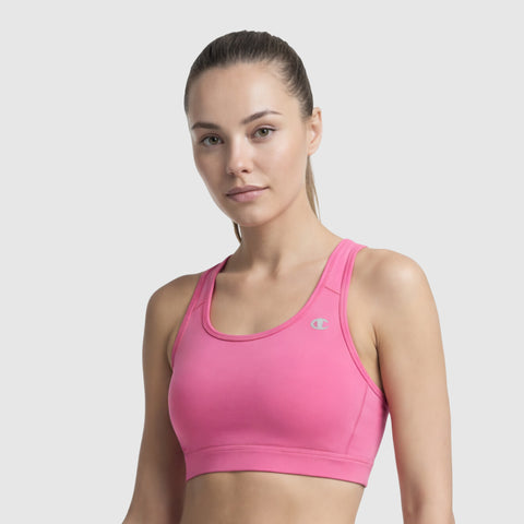 A woman with light skin and brown hair pulled back wears a bright pink Champion Compression Sports Bra featuring moderate support and a small C logo on the left strap, standing against a plain light gray background.