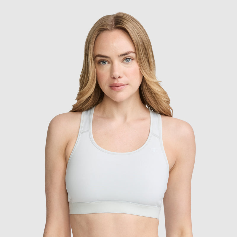 A woman with long blonde hair wears the Champion Compression Sports Bra, featuring a signature C logo and offering moderate support. She looks forward with a neutral expression against a plain light gray background. The bra’s moisture-wicking fabric helps keep her comfortable throughout her workout.