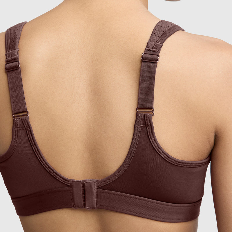 A person is shown from the back wearing the Champion Spot Comfort High-Impact Sports Bra, C Logo in brown, featuring adjustable straps and a hook-and-eye closure, set against a plain light background.