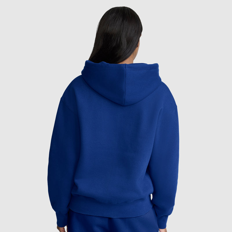 A person with long dark hair, shown from the back against a plain light gray background, is wearing a royal blue Champion Powerblend Fleece Zip-Up Hoodie, C Logo, paired with matching pants.