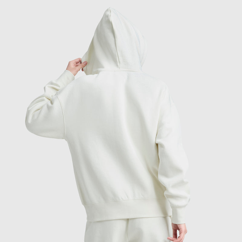Person wearing a Champion Powerblend Fleece Zip-Up Hoodie, C Logo, in white with the hood up and holding the hood's edge, facing away from the camera against a plain light background.