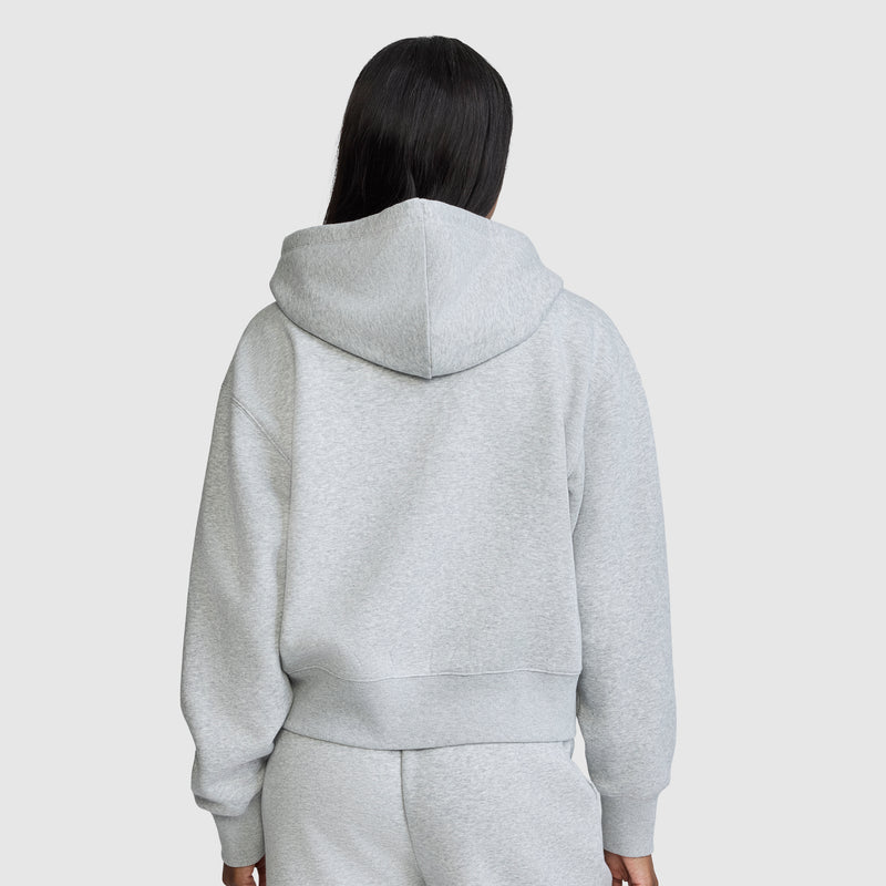 A person with long dark hair wears the Champion Cropped Zip-Up Hoodie in light gray, paired with matching sweatpants, facing away from the camera against a plain, light background.