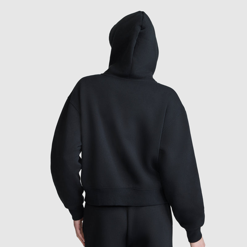 A person is shown from the back wearing a black Champion Cropped Zip-Up Hoodie and black pants, standing against a plain light gray background.