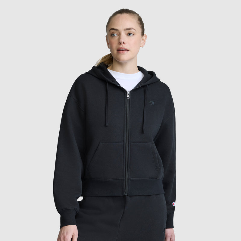 A woman wearing the Champion Cropped Zip-Up Hoodie and matching pants stands against a plain light gray background, looking slightly to the side.