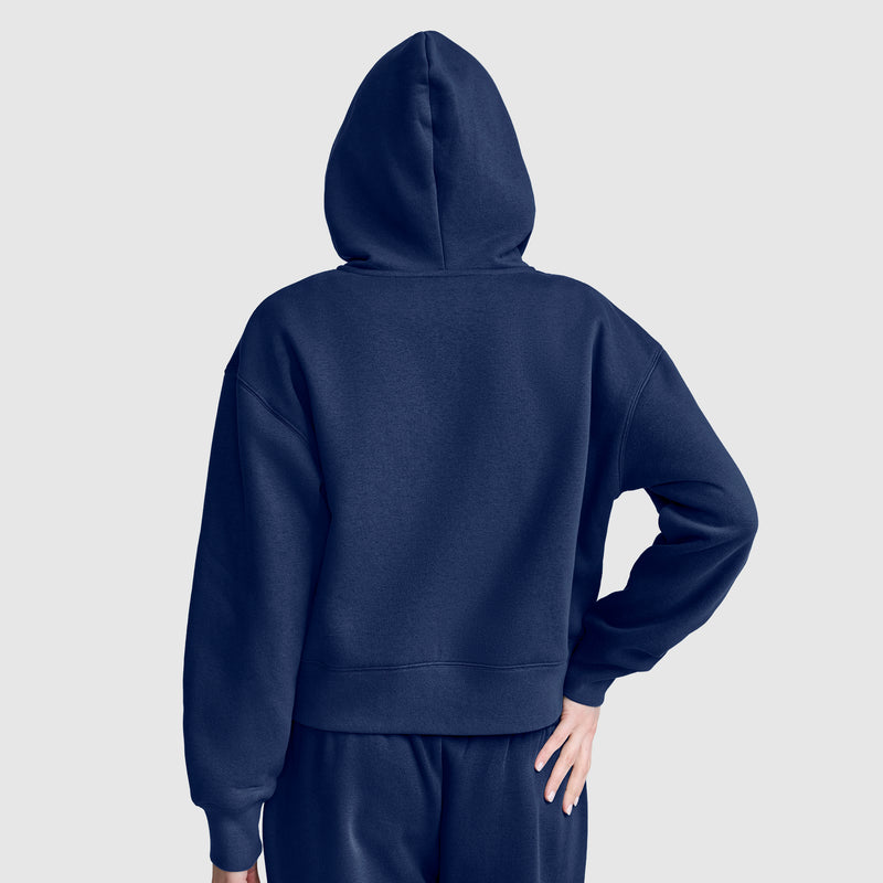 A person wearing a Champion Cropped Zip-Up Hoodie and matching sweatpants stands with one hand on their hip, facing away from the camera against a plain light gray background.