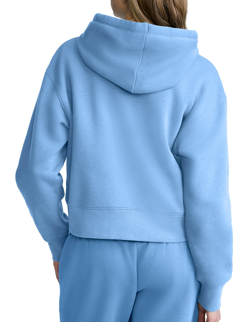 A person is shown from the back wearing a light blue Champion Cropped Zip-Up Hoodie and matching sweatpants. The hood is down, and the fleece outfit looks soft and comfortable.