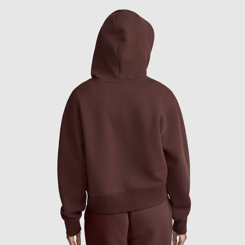 A person wearing a brown Champion Cropped Zip-Up Hoodie and matching pants stands facing away from the camera against a plain light gray background.