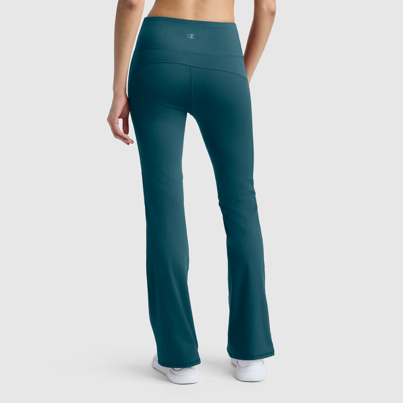A person is shown from the back, standing against a plain light gray background, wearing Champion Soft Touch Flare Leggings with anti-odor technology and a C logo in teal, paired with white sneakers.
