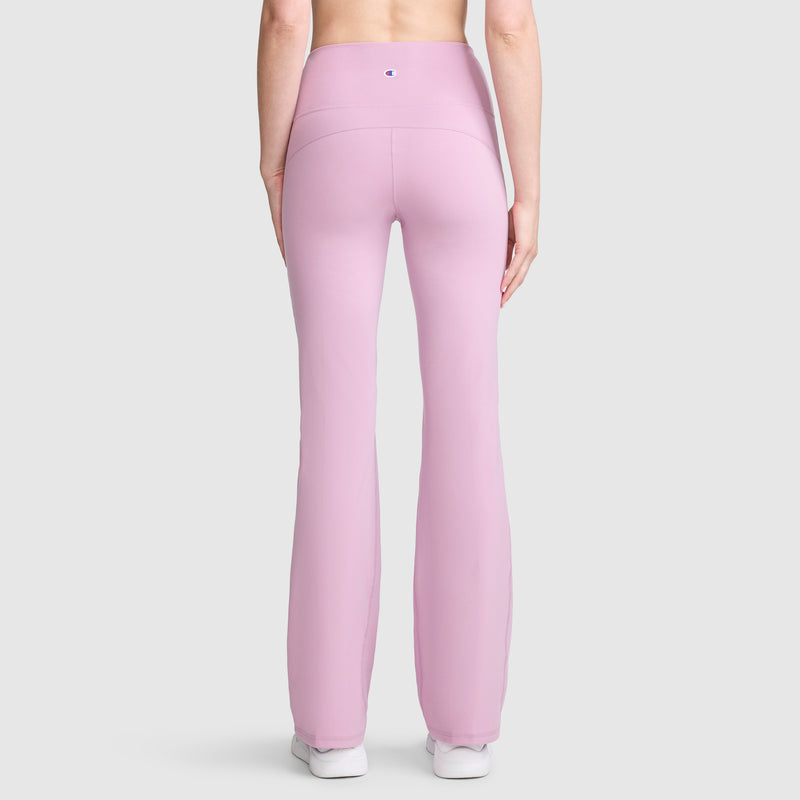A person is shown from the back against a plain light gray background, wearing Champion Soft Touch Flare Leggings in a high-waisted, light pink style featuring anti-odor technology and the signature C Logo—perfect workout leggings for women—paired with white shoes.