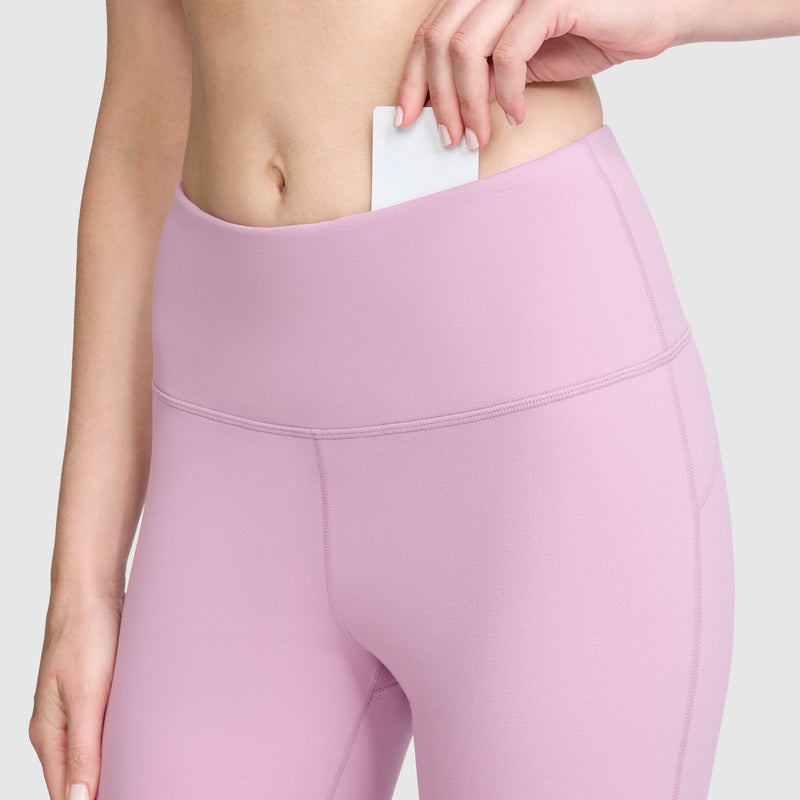 A person wearing Champion Soft Touch Flare Leggings with the C Logo, featuring anti-odor technology, slips a white card into the waistband pocket, with the focus on their hand and midsection.