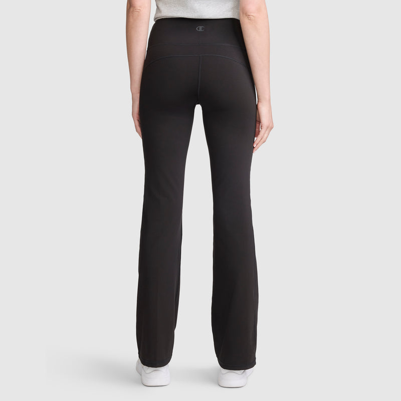 A person is seen from the back wearing Champion’s Soft Touch Flare Leggings with anti-odor technology and C Logo in black, paired with a light gray top, standing against a plain light background.