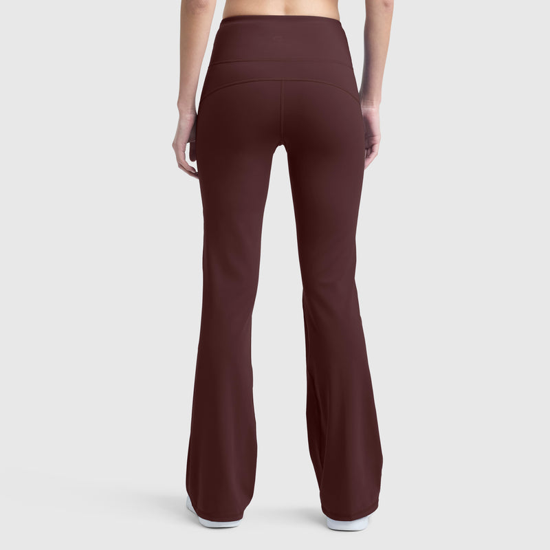 A person is shown from the back wearing Champion Soft Touch Flare Leggings, featuring a high-waisted fit in maroon with anti-odor technology and a C logo, paired with white shoes against a plain light gray background.