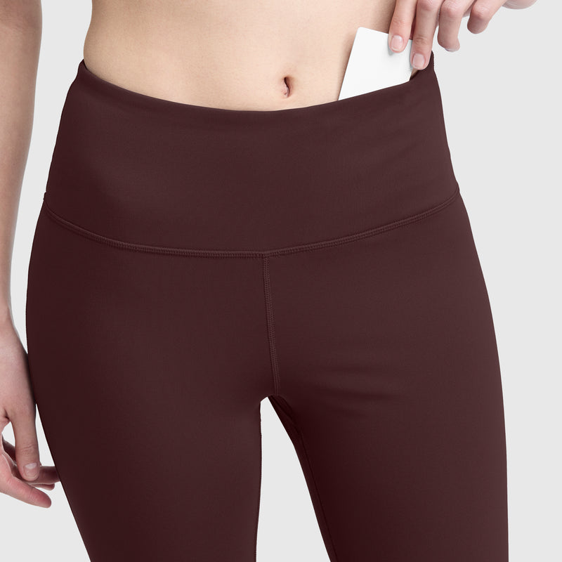 A person slips a card into the discreet waistband pocket of Champion Soft Touch Flare Leggings, featuring anti-odor technology and a signature C logo, highlighting the pocket’s functionality. The image centers on the midsection, keeping the person’s face out of view.