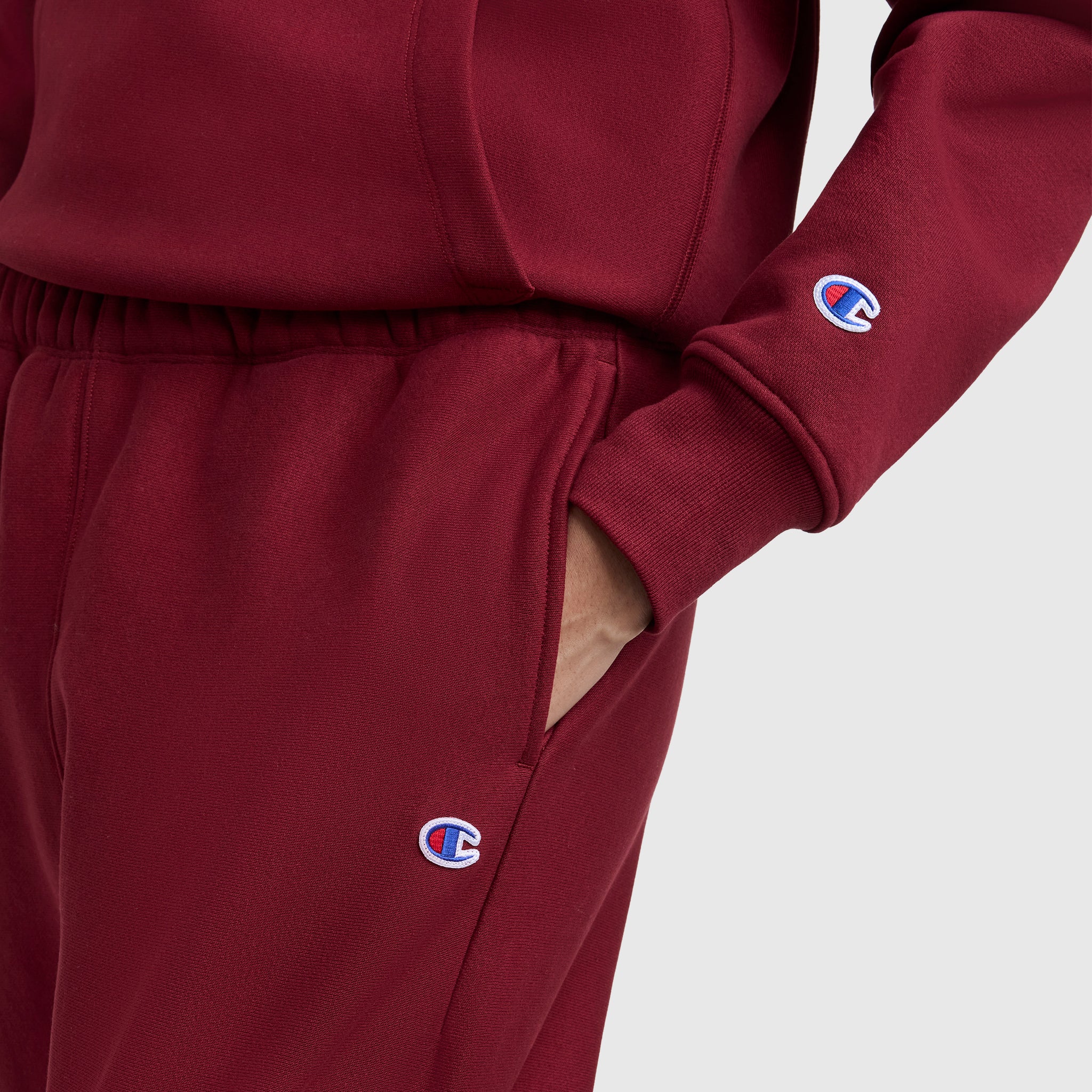 A person wears Champion Essentials Reverse Weave Cinched Bottom Sweatpants and a matching top, with their hand in the pocket. The Champion logo is visible on the sleeve and pants for a classic athletic look.