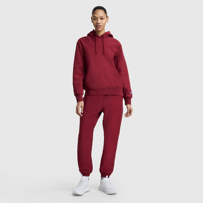 A person faces forward, wearing a matching maroon hoodie and Champion Essentials Reverse Weave Cinched Bottom Sweatpant with white sneakers, against a plain light gray background.