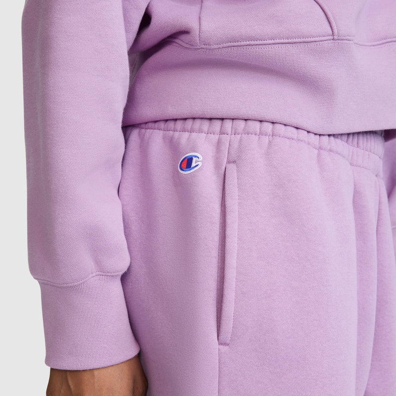 A person is shown from the torso to upper legs, against a plain background, wearing a lavender Powerblend fleece sweatshirt and matching Champion Powerblend Oversized Sweatpants featuring a small C logo above the pocket.