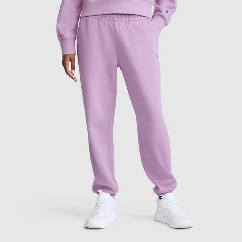 A person wearing Champion’s Powerblend Oversized Sweatpants with the C Logo in light purple, along with a matching soft fleece sweatshirt and white sneakers, stands against a plain white background. Only the body from the shoulders down is visible.