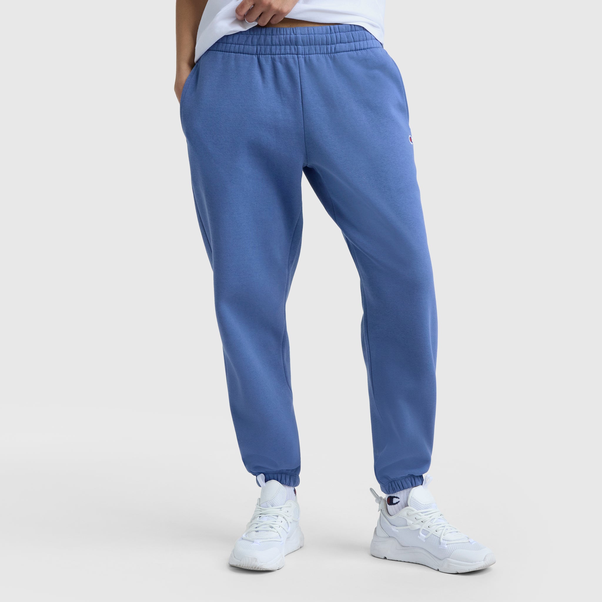 Model wears Champion Powerblend Oversized Sweatpants with C Logo in blue, paired with white sneakers, hands in pockets—showcased from the waist down on a light background for effortless women’s loungewear style.