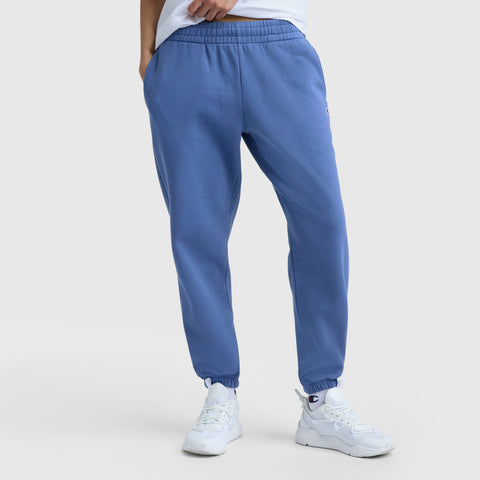 Model wears Champion Powerblend Oversized Sweatpants with C Logo in blue, paired with white sneakers, hands in pockets—showcased from the waist down on a light background for effortless women’s loungewear style.