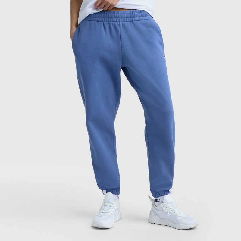 Model wears Champion Powerblend Oversized Sweatpants with C Logo in blue, paired with white sneakers, hands in pockets—showcased from the waist down on a light background for effortless women’s loungewear style.