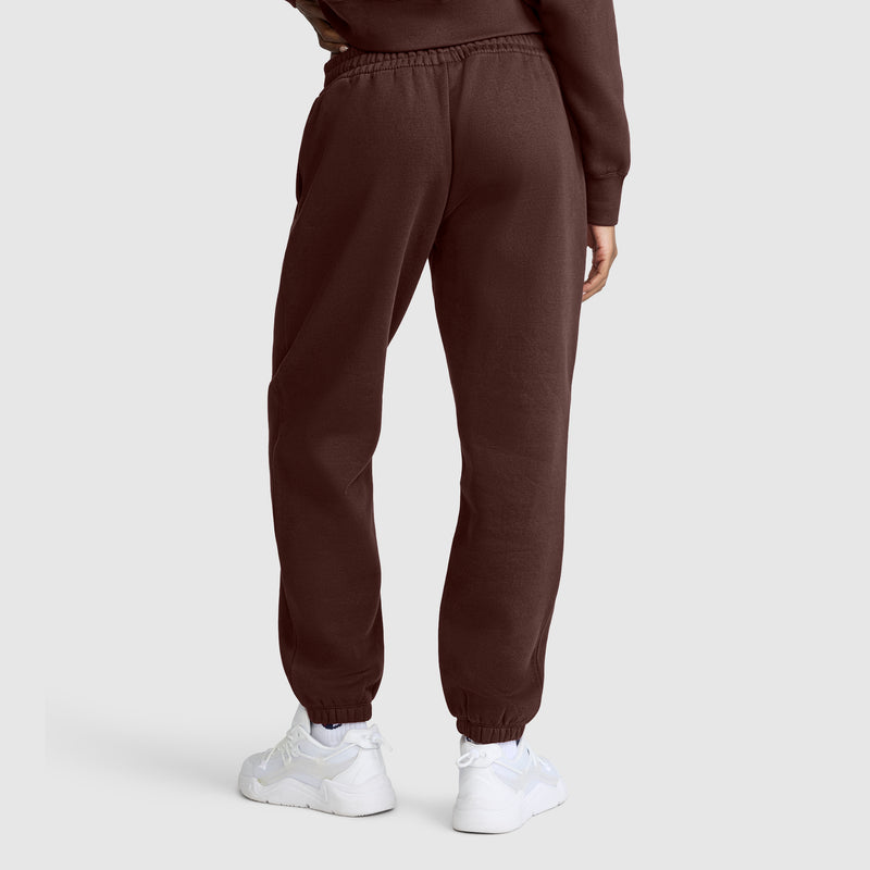 A person wearing Champion Powerblend Oversized Sweatpants with the C Logo in dark brown and white sneakers, photographed from the back against a plain light gray background.