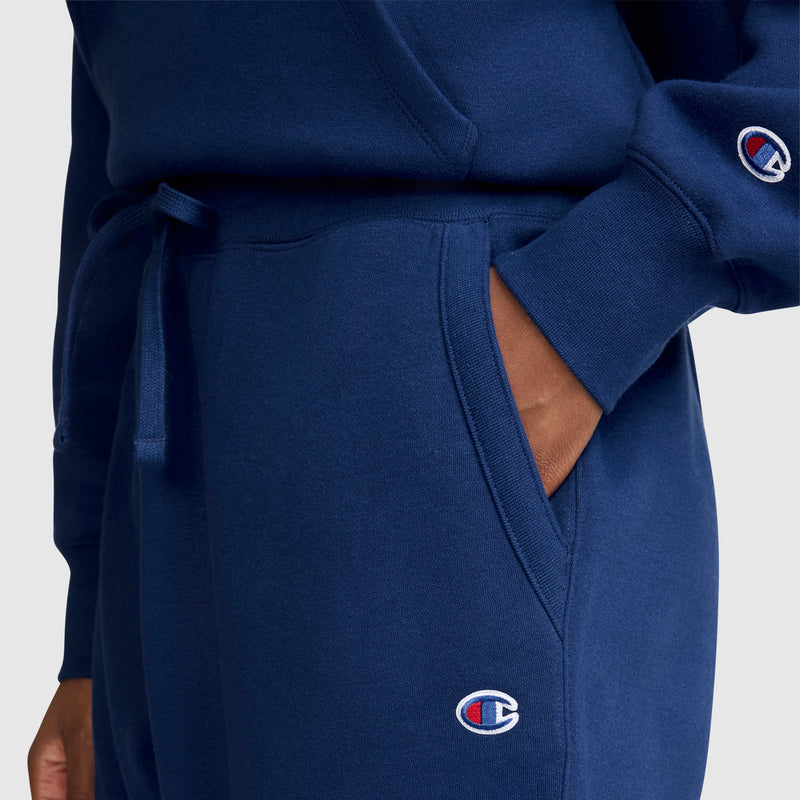 A person is wearing a matching blue Champion sweatshirt and Champion Powerblend Joggers, C Logo, with hands in the pocket. Both garments feature the Champion logo, highlighting the cozy style of Powerblend fleece joggers.