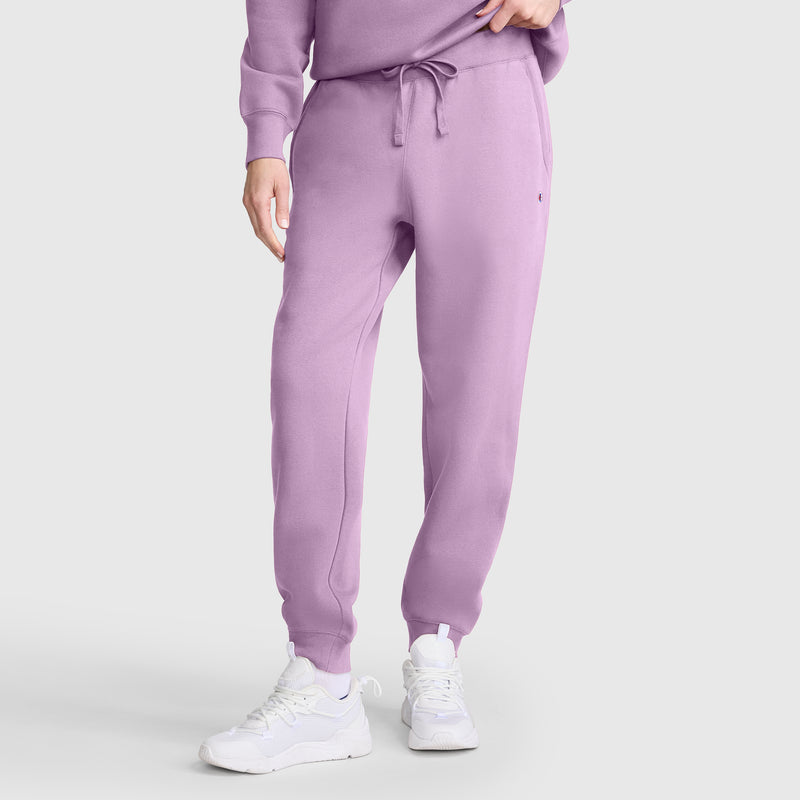 A person wears Champion Powerblend Joggers, C Logo in lavender with a matching sweatshirt and white athletic shoes, standing against a plain light background. Only the lower body and part of one arm are visible—perfect for showcasing your favorite Champion women's joggers in a relaxed yet stylish way.