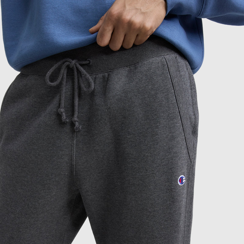 A person is wearing blue and dark gray Champion Powerblend Straight Hem Sweatpants, made from midweight fleece with a drawstring waist and a small Champion logo on the left thigh.