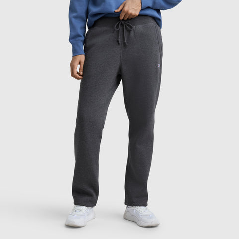 A person stands against a white background wearing a blue sweatshirt, white sneakers, and dark gray Champion Powerblend Straight Hem Sweatpants. The individual’s face is not visible.