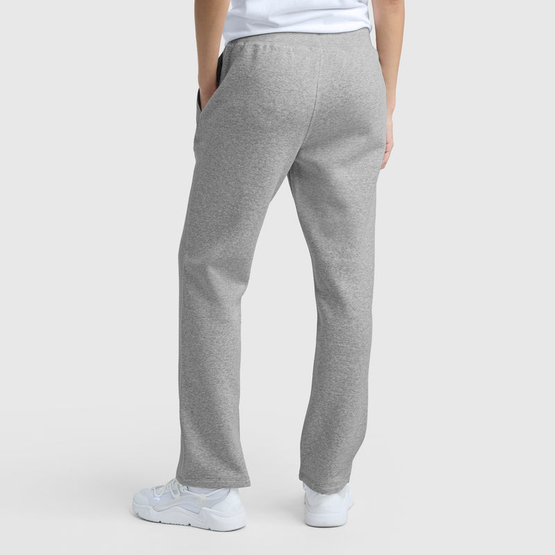 A person stands with their back to the camera in light gray Champion Powerblend Straight Hem Sweatpants, paired with white sneakers and a white t-shirt, against a plain light gray background, showcasing the pants’ fit from behind.