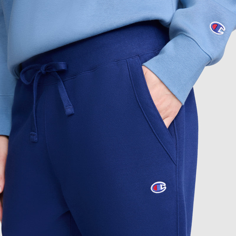 Person wearing slim fit blue Champion Powerblend Straight Hem Sweatpants and a light blue Champion sweatshirt, with one hand in the pants pocket. Both garments, crafted from midweight fleece, feature the distinctive Champion logo.