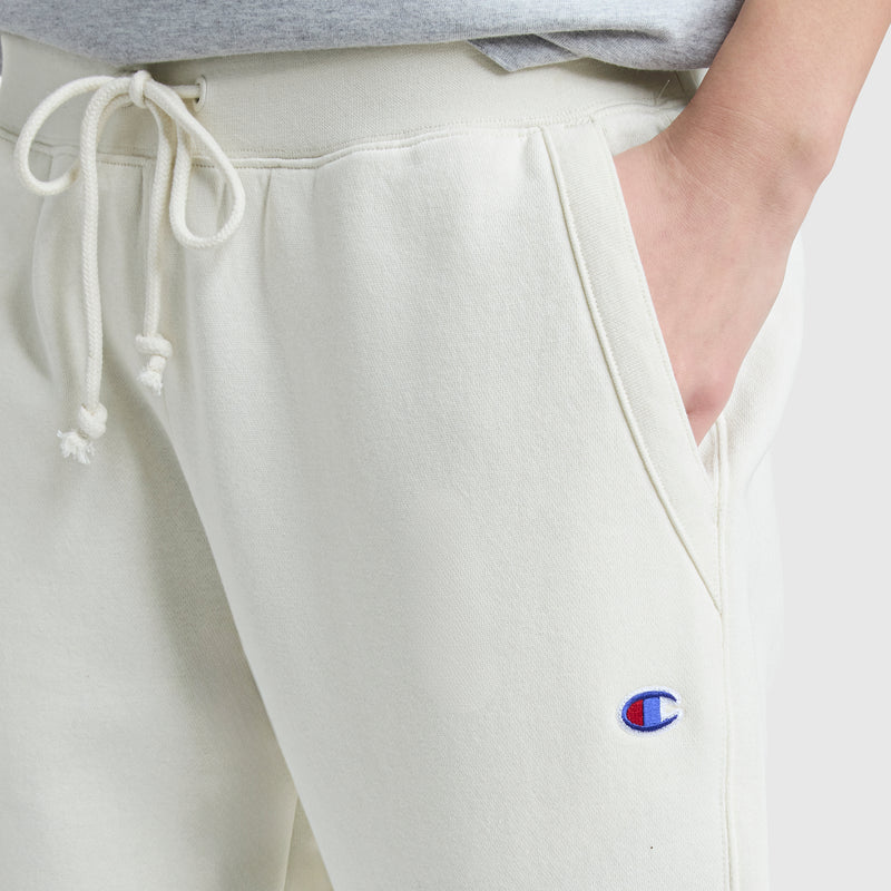 Someone wears off-white Champion Powerblend Straight Hem Sweatpants made from soft midweight fleece, featuring a drawstring waist, relaxed fit, visible logo near the pocket, and a straight hem. One hand rests in the pocket.