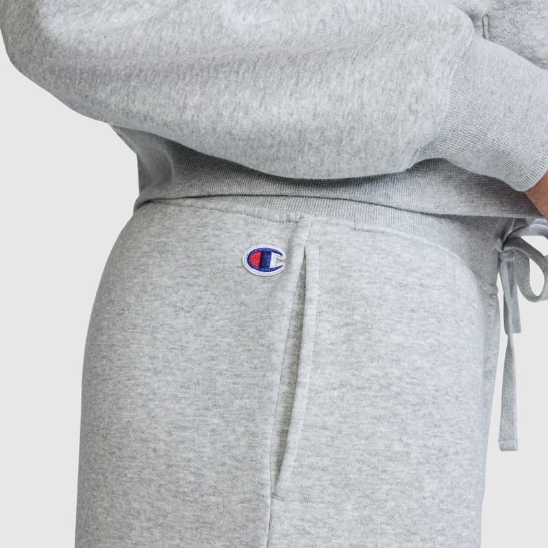 A person is wearing light gray Champion Wide Leg Fleece Sweatpants, featuring the signature C Logo near the pocket, paired with a matching sweatshirt. The comfortable and casual outfit is perfect for lounging in cozy women’s fleece sweatpants from Champion.