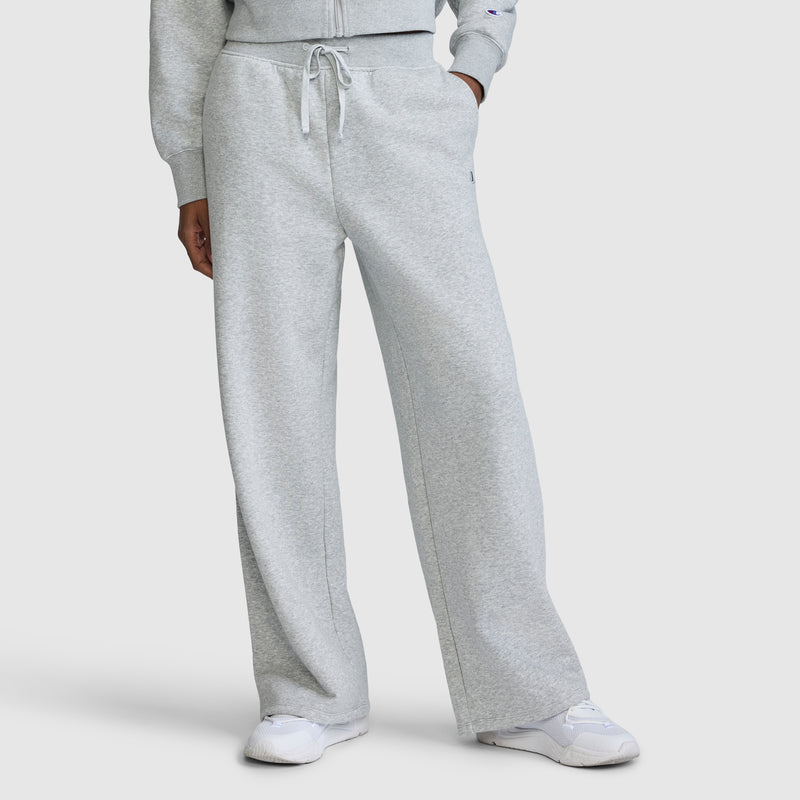 A person is wearing Champion's Wide Leg Fleece Sweatpants with the C Logo in light gray, paired with a matching sweatshirt and white sneakers. The photo is cropped from the shoulders down to showcase the relaxed fit and comfortable style of these sweatpants.