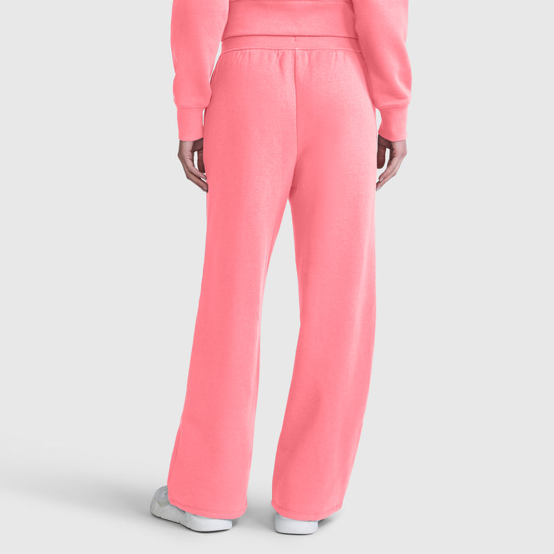A person is seen from the back wearing bright pink Champion Wide Leg Fleece Sweatpants with a C Logo, paired with a matching sweatshirt. The sweatpants have a loose fit and straight-leg cut, similar to wide leg styles. The outfit is completed with white sneakers.