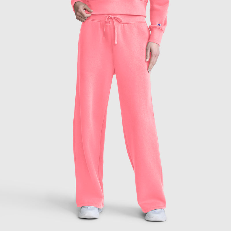 A person is wearing Champion Wide Leg Fleece Sweatpants, C Logo, in bright pink—paired with a matching pink sweatshirt and white sneakers—standing against a plain white background.