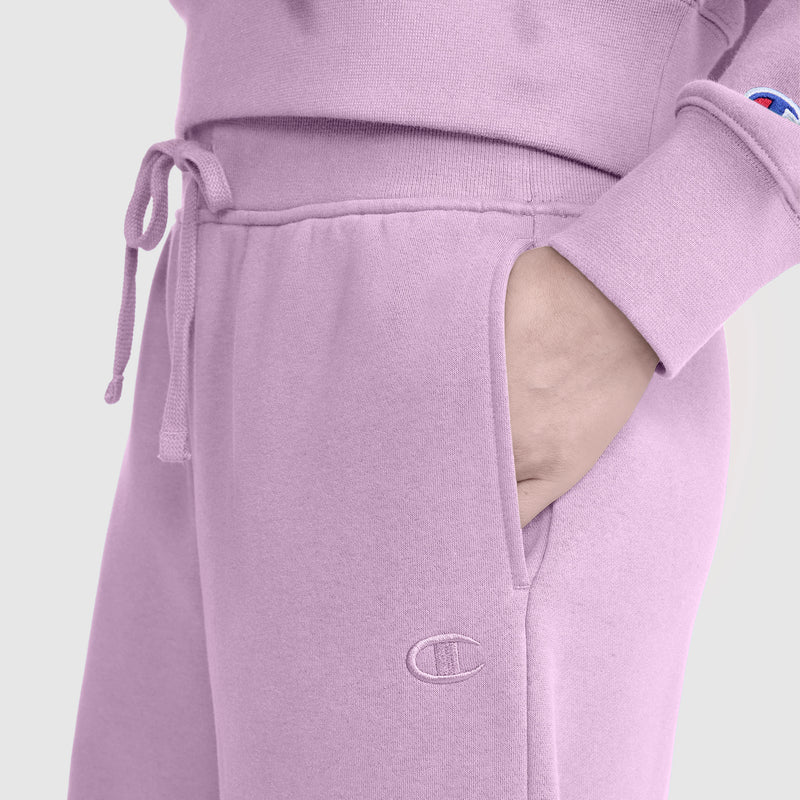 A person wearing light purple Champion Wide Leg Fleece Sweatpants, C Logo, and a matching sweatshirt has one hand in their pocket. The outfit features drawstrings, the signature Champion logo, and highlights the cozy style of these women's wide leg fleece sweatpants.