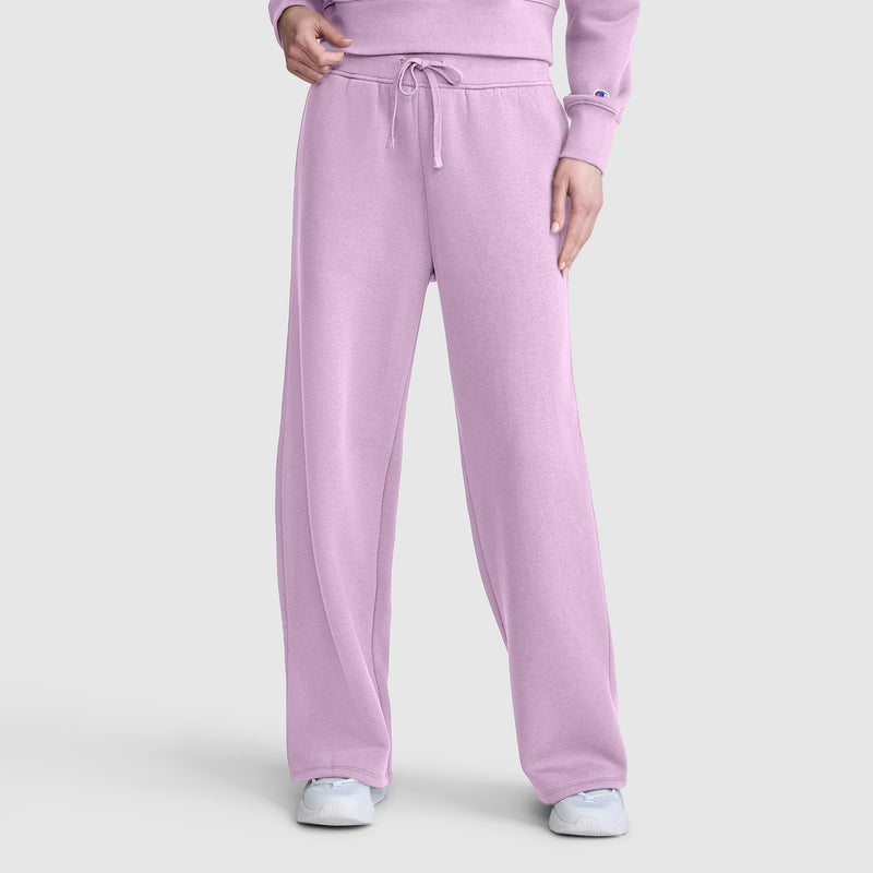 A person is wearing Champion Wide Leg Fleece Sweatpants with a C Logo in light purple, paired with a matching sweatshirt and white sneakers, standing against a plain gray background.