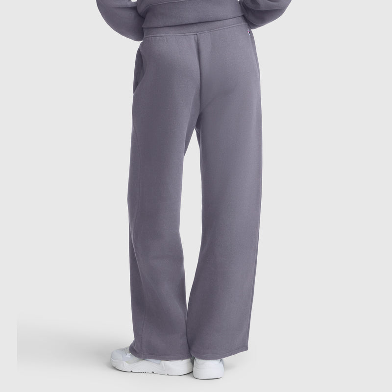 A person is shown from the back, hands in pockets, wearing Champion Wide Leg Fleece Sweatpants with the C Logo in purple and white sneakers, set against a plain white background.