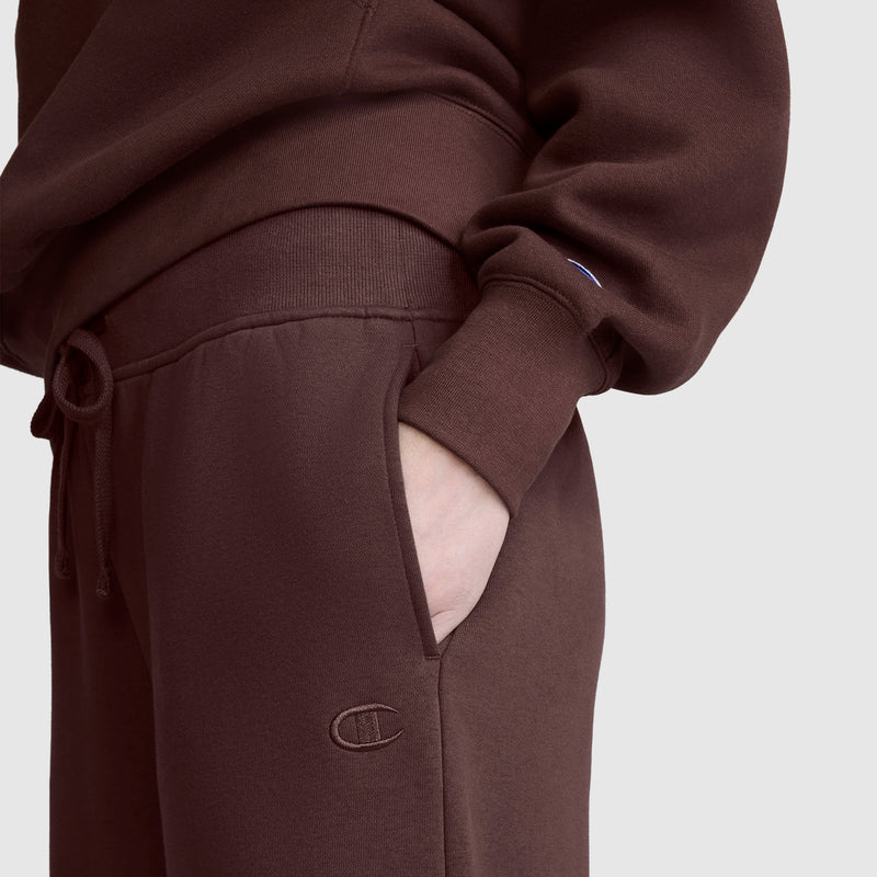 A person is wearing a brown sweatshirt and matching Champion Wide Leg Fleece Sweatpants with a hand in the pocket; the iconic C logo is visible on these comfortable women’s cotton fleece pants.