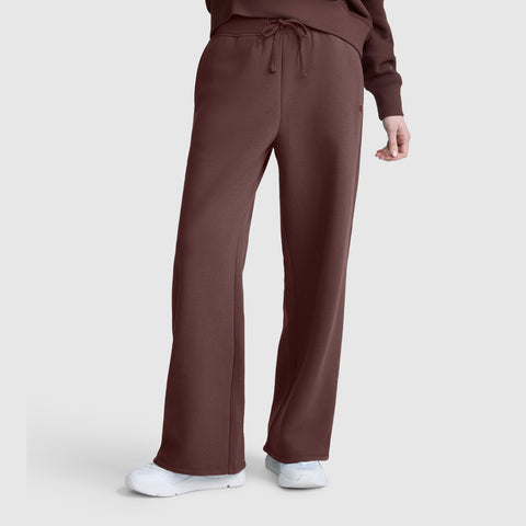 A person models the Champion Wide Leg Fleece Sweatpants, featuring the C Logo, paired with a matching brown top and white sneakers against a plain light background.