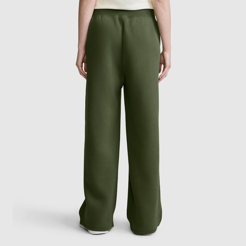 A person is shown from the back, standing against a plain light gray background, wearing the Champion Wide Leg Fleece Sweatpants with C Logo in dark green and a white shirt.