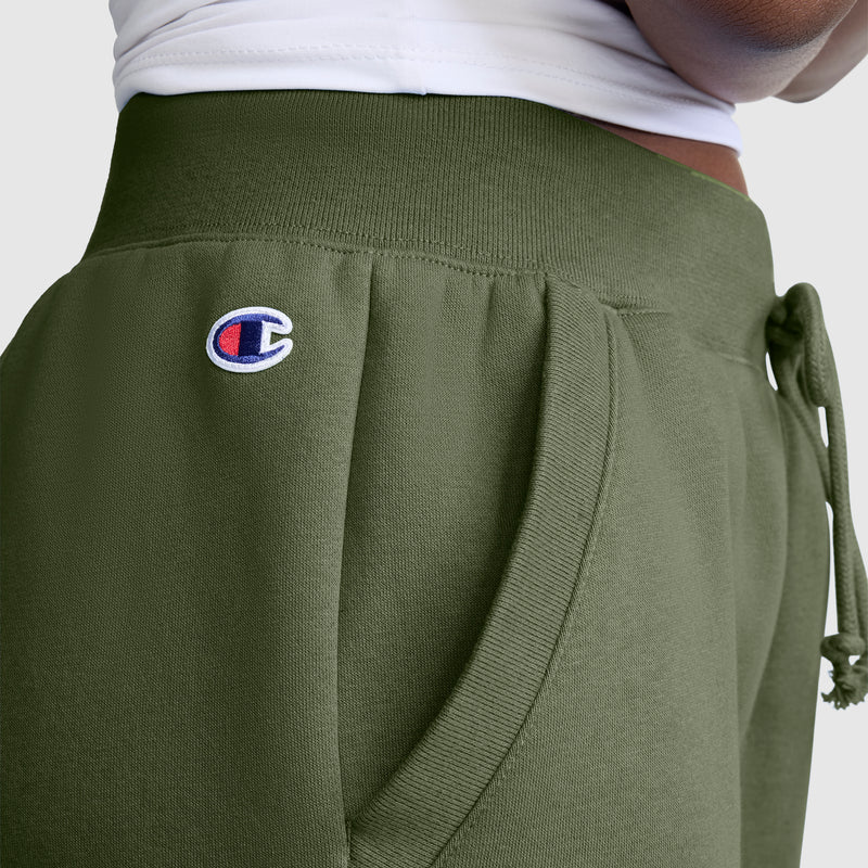 Close-up of a person wearing Champion Powerblend Joggers with the Classic Script Logo in olive green, featuring a white waistband and their hand resting in the pocket—highlighting these comfortable, everyday pants.
