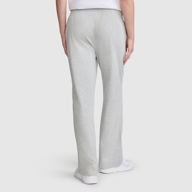 A person wearing Champion Lightweight Lounge Pants, C Logo in light gray jersey cotton and white sneakers is shown from the back, standing against a plain white background. These pants offer superior comfort and style with Champion quality craftsmanship.